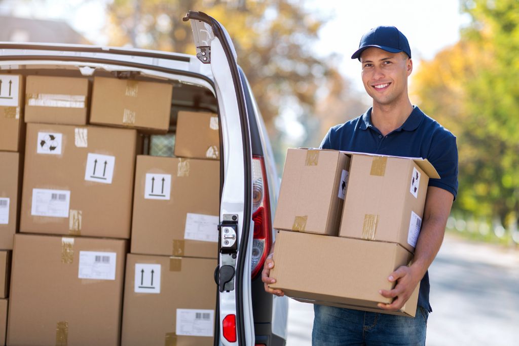 A delivery man is holding   boxed packages