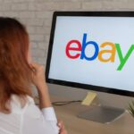 A woman sitting infront of a computer with an ebay logo on screen